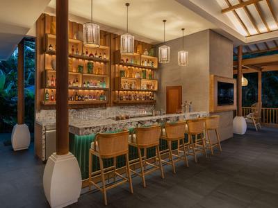 Area bar dell'hotel moderna con accenti in legno e pietra e sgabelli sotto lampade a sospensione eleganti.