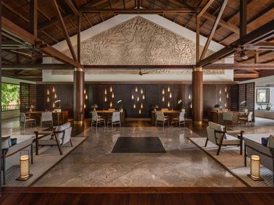 Ampia hall dell'hotel con travi in legno, poltrone, tappeti e illuminazione calda.