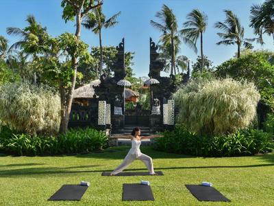 Persona pratica yoga su un prato verde con vegetazione tropicale e un cancello ornato.