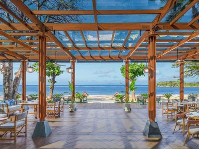 Otevřená krytá jídelní část s výhledem na moře a bílým nábytkem.