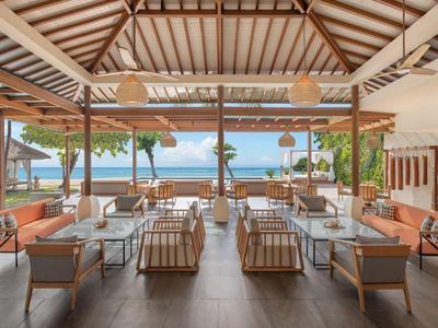 Area lounge aperta con mobili in legno e vista sull'oceano in un resort tropicale.