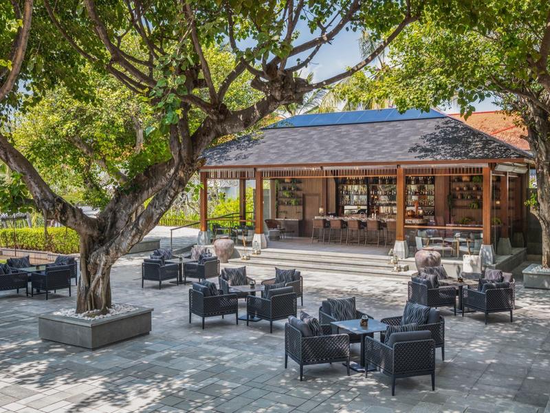 Venkovní posezení s zahradním nábytkem pod stromy před otevřeným dřevěným pavilonem v hotelu