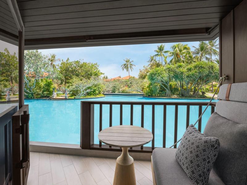 Pohled z terasy s pohovkou a stolem na bazén a tropické rostliny.