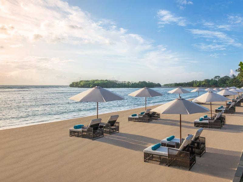 Západ slunce na pláži s lehátky a slunečníky na dřevěné terase vedle palm.