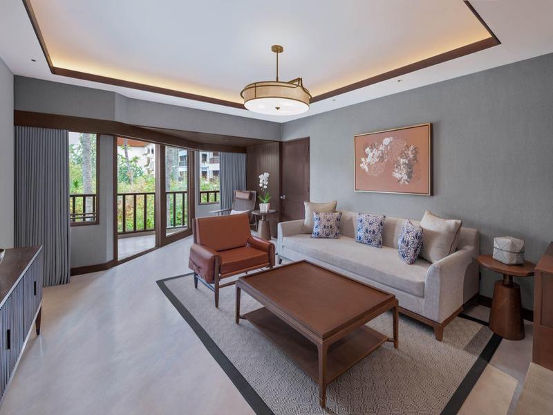 Moderně zařízený obývací pokoj se šedými stěnami, pohovkou, křesly a velkým oknem s výhledem do zeleně.