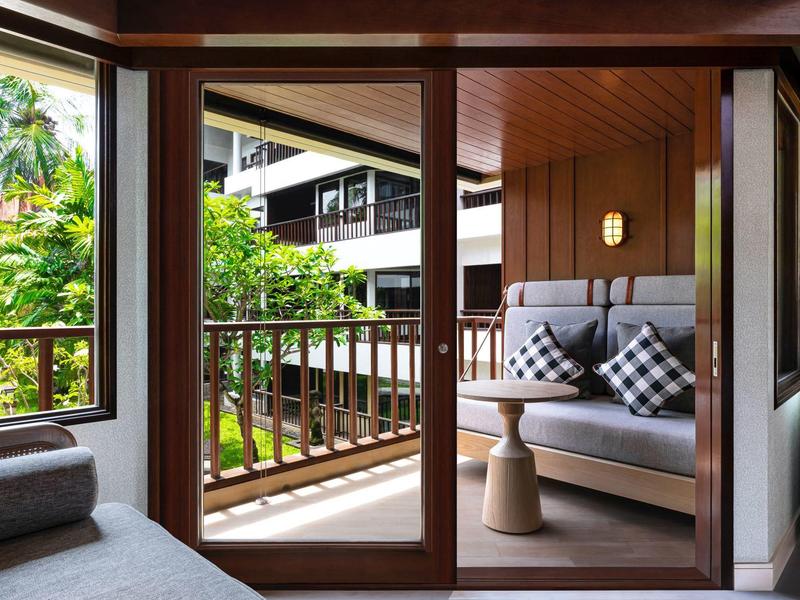 Hotelový balkon s posezením s výhledem na zelené listí a moderní architekturu.