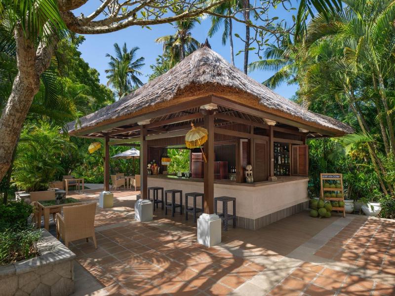 Venkovní bar se slaměnou střechou a posezením v tropické zahradě.