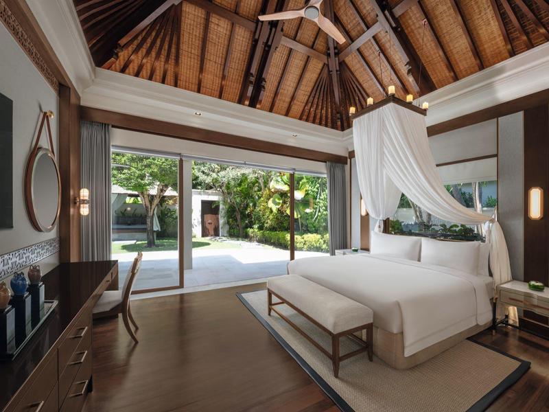 Luxusní ložnice s otevřenou dřevěnou střechou, postelí s moskytiérou a výhledem na terasu a zahradu.