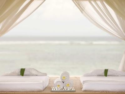 Dos camillas de spa con toallas frescas y vista al mar bajo un dosel blanco.