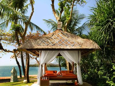 Lounge cubierta con sofá naranja, rodeada de palmeras con vista al mar en la playa.