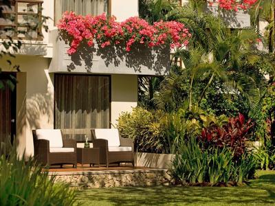 Área de terraza con dos sillas frente a un balcón con flores rojas y abundante vegetación.