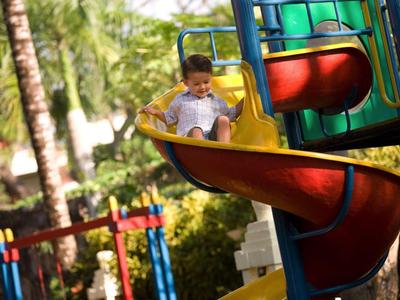 Un niño desliza por un tobogán en espiral colorido en un área exterior soleada con palmeras.