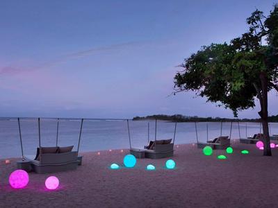 Playa con bolas coloridas iluminadas y tumbonas bajo árboles al atardecer.