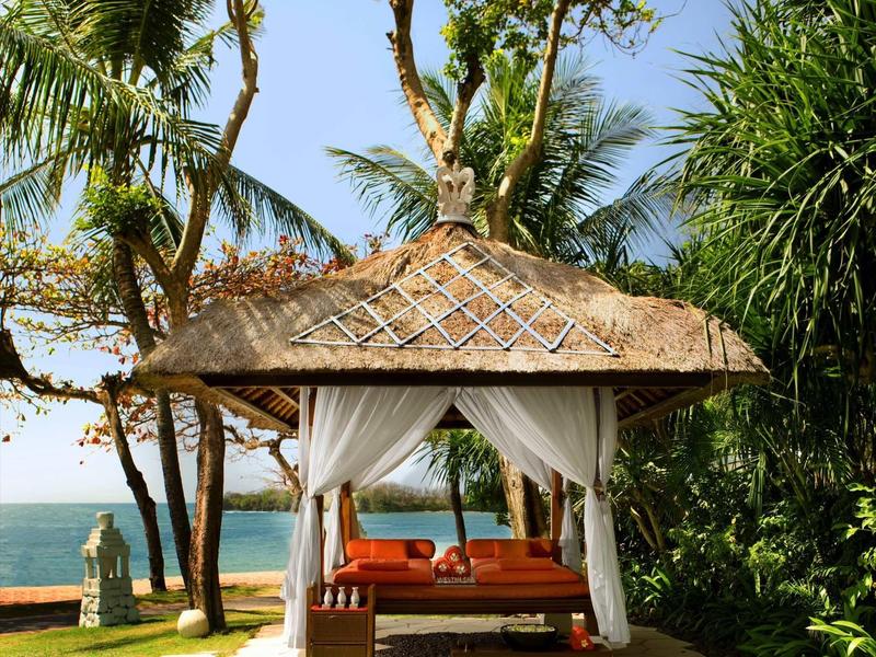 Lounge cubierta con sofá naranja, rodeada de palmeras con vista al mar en la playa.