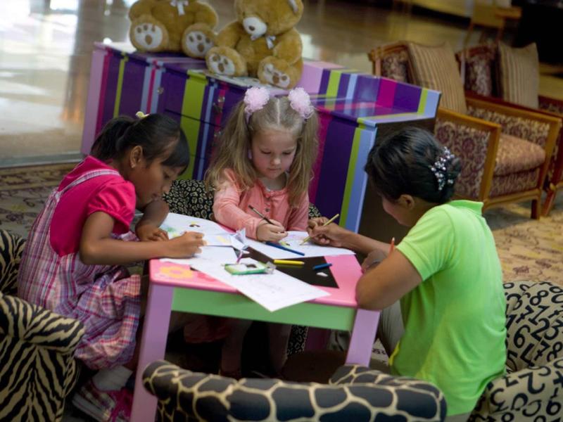 Tres niños sentados alrededor de una mesa pequeña dibujan en la sala de un hotel.