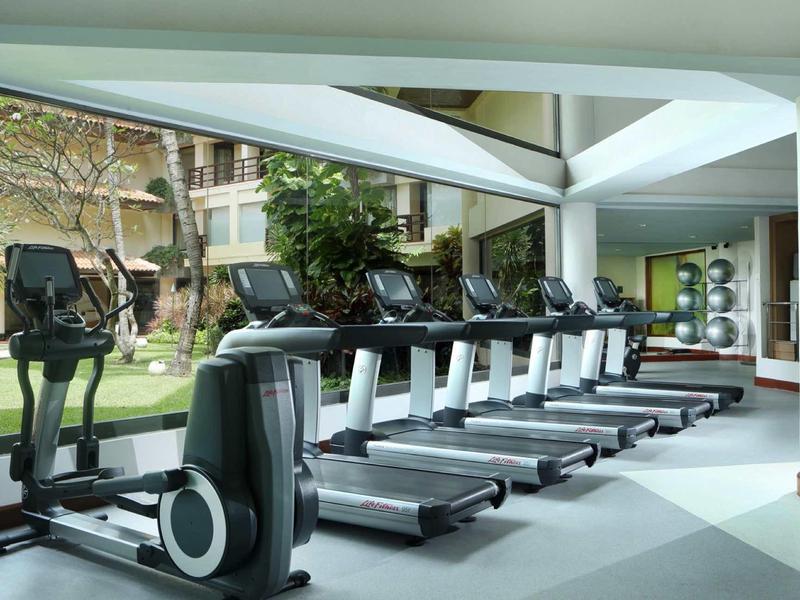 Gimnasio moderno con varias cintas de correr y elíptica junto a grandes ventanas.