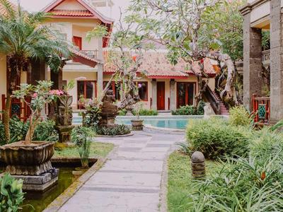 Udržovaná zahrada s chodníkem, stromy a bazénem před tradiční budovou.