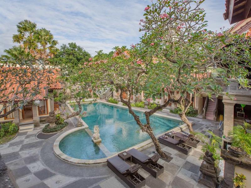 Zona piscina tranquilla con alberi e lettini in un hotel con architettura tradizionale.