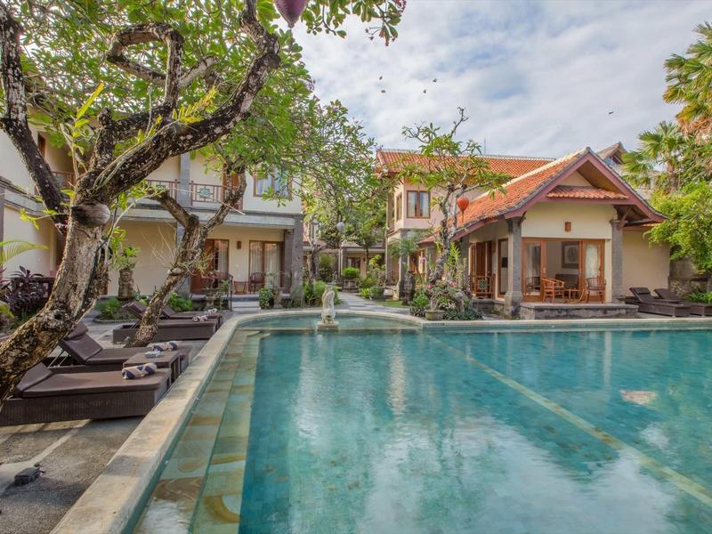 Una piscina tranquilla con lettini e alberi in un giardino dell'hotel con edifici tradizionali.
