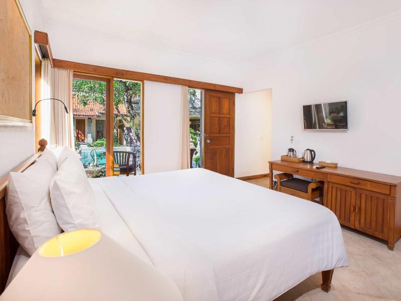 Camera d'hotel luminosa con letto grande, TV a muro e mobili in legno.