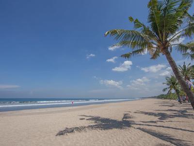Weißer Sandstrand mit Palmen und blauem Himmel, das Meer im Hintergrund mit kleinen Wellen.