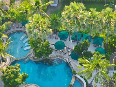 Vogelperspektive auf blauen Pool mit Palmen und grünen Schirmen umgeben von Gartenanlagen.