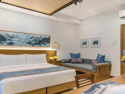 Modernes Hotelzimmer mit Bett, Sofabereich und Holzdetails in hellen Farben.