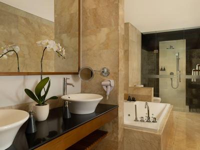 Elegantes Hotelbadezimmer mit zwei Waschbecken, Badewanne und regendusche mit cremefarbenen Fliesen.