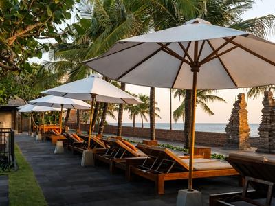 Mehrere Sonnenliegen mit weißen Sonnenschirmen neben einem tropischen Garten mit Blick aufs Meer.