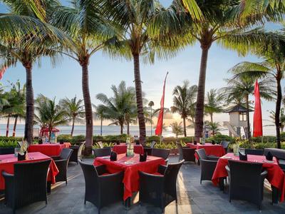 Terrasse mit schwarzen Möbeln und roten Kissen unter Palmen mit Blick aufs Meer bei Sonnenuntergang.