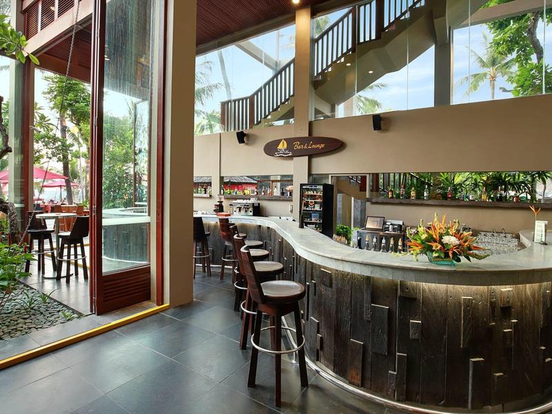 Moderne hotelbar met gebogen bar en barkrukken, omgeven door grote ramen en planten.