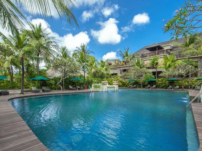 Uitnodigend buitenzwembad met palmbomen en ligstoelen onder een blauwe lucht.