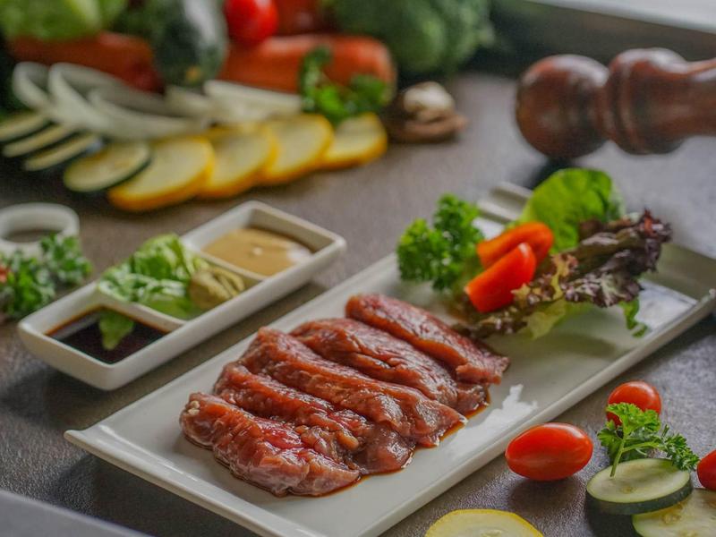 Verschillende plakjes gerookte worst op een bord met kruiden en sauzen.