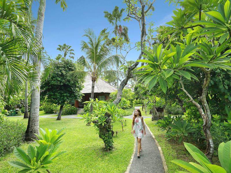 Vrouw loopt op een pad door een weelderige tropische tuin naar een bungalow.