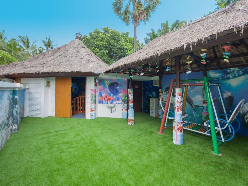 Binnenplaats met groen kunstgras, schommel en bungalow met rieten dak.