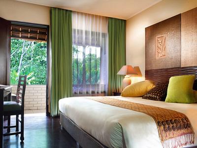 Habitación de hotel acogedora con cama doble, cortina verde y vista a un balcón con árboles.