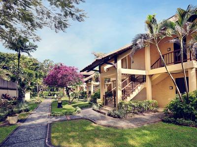 Edificio de hotel de dos pisos con palmeras y senderos de jardín bien cuidados bajo un cielo azul.