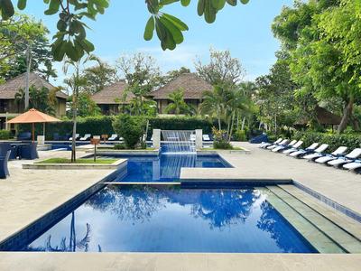 Una piscina exterior moderna con tumbonas y árboles en un jardín de hotel.