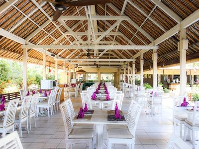 Restaurante abierto y luminoso con muebles blancos y servilletas moradas bajo un techo de madera.