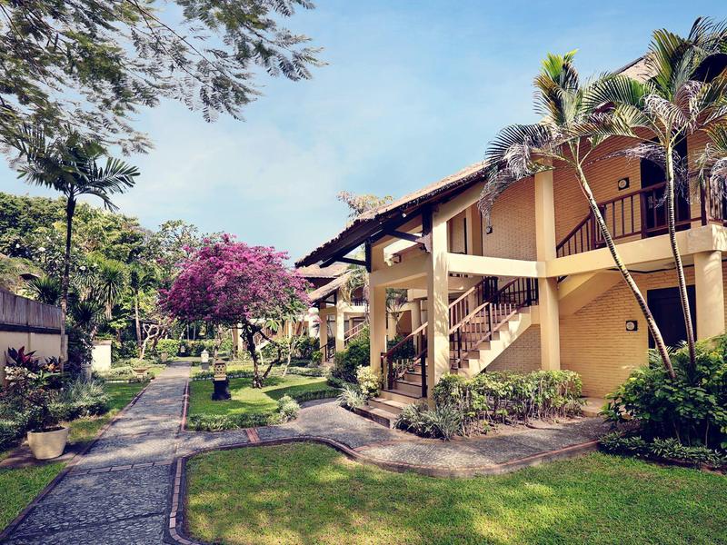 Edificio de hotel de dos pisos con palmeras y senderos de jardín bien cuidados bajo un cielo azul.