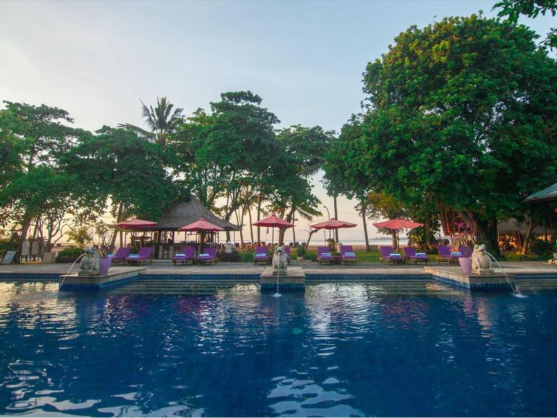 Gran piscina con tumbonas y pabellones, rodeada de árboles verdes al atardecer.