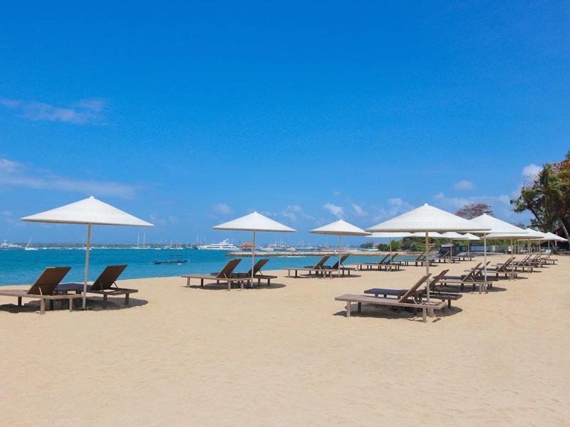 Playa con tumbonas y sombrillas blancas bajo un cielo azul junto al mar.