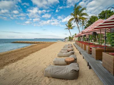 Strand mit Sand, Sitzsäcken und Strohsonnenschirmen neben einer Strandbar unter blauem Himmel.