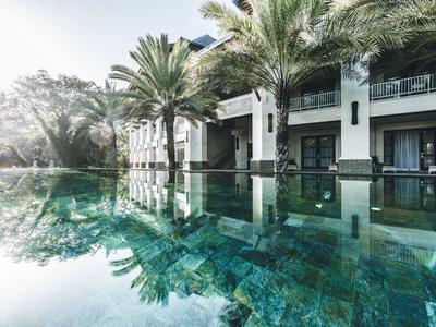 Moderner Hotelpool mit klaren Wasserflächen, Palmen und weißem Gebäude im Hintergrund.
