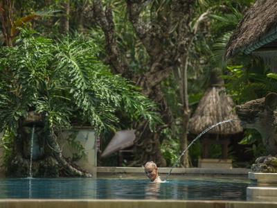 Frau im Pool, umgeben von dichter, grüner Dschungelvegetation und traditionellem Strohdach.