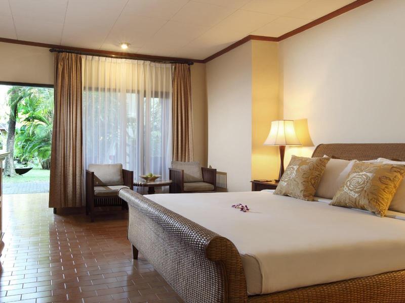 Elegant hotelkamer met groot bed, bank, tv en toegang tot de tuin.