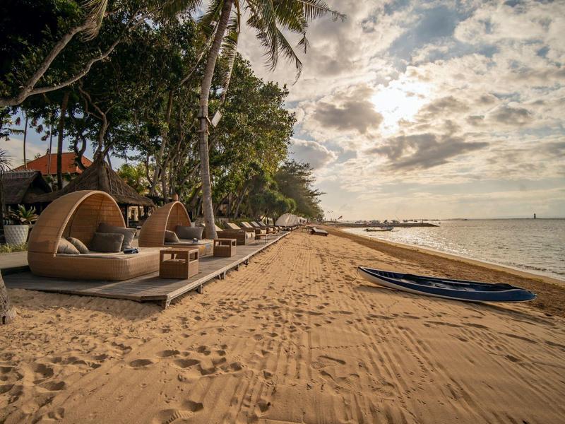 Een rustig strand met comfortabele ligstoelen en palmbomen in het ochtendlicht.