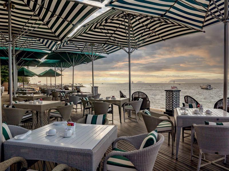 Overdekt terras met tafels en stoelen met uitzicht op zee bij zonsondergang.