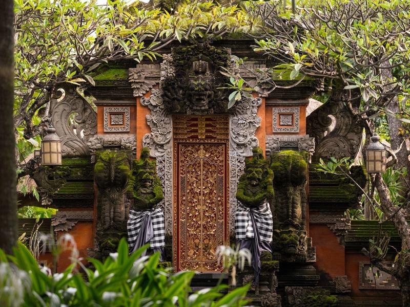 Traditionele Balinese stenen tempel met gebeeldhouwde deuren omringd door groen.