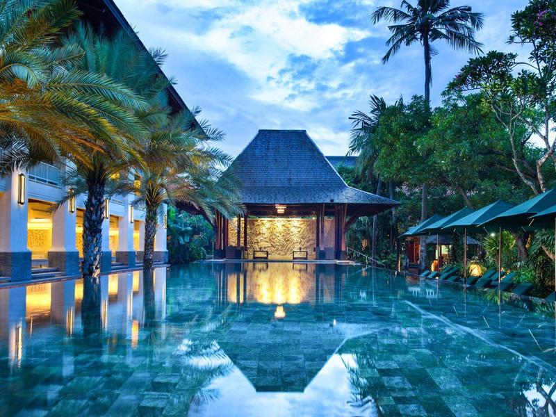 Luxe zwembad met palmen en verlicht paviljoen bij schemering.